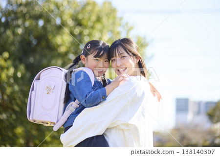 一個背著書包的小女孩和她的媽媽擁抱在一起。 一個背著書包的小女孩和她的媽媽擁抱在一起。 138140307