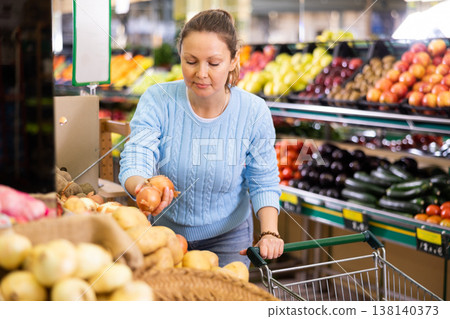 Positive middle-aged female buyer choosing onion in supermarket Positive middle-aged female buyer choosing onion in supermarket 138140373