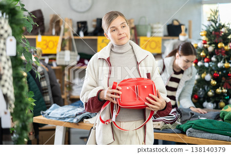 Uncertain young woman choosing handbag in clothing store Uncertain young woman choosing handbag in clothing store 138140379