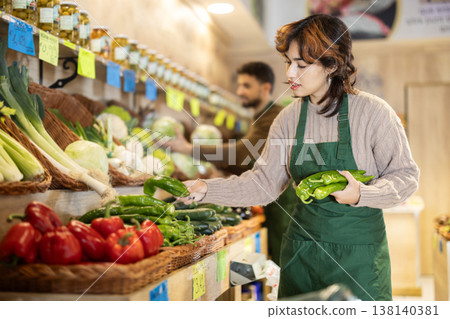 Young woman seller puts peppers in store Young woman seller puts peppers in store 138140381