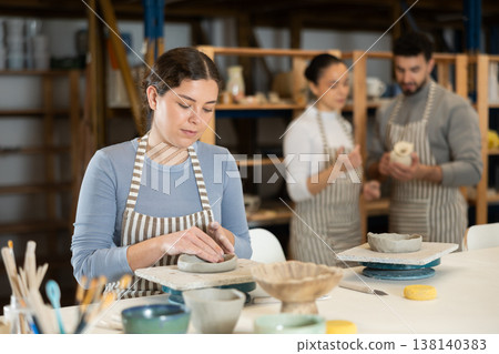 Girl sitting at table, busy making products from raw clay Girl sitting at table, busy making products from raw clay 138140383