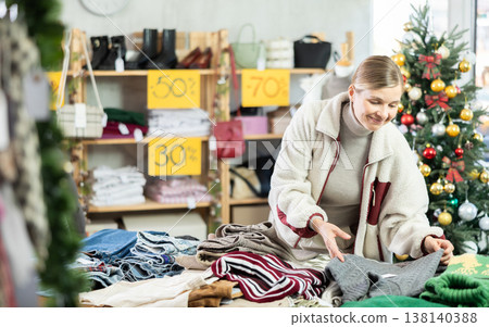 Positive young woman choosing sweater in clothing store 138140388