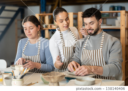 Girl master leaned over to man and helps to sculpting from clay Girl master leaned over to man and helps to sculpting from clay 138140406
