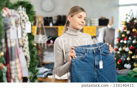 Woman client looks at products in store, choose closely ladys jeans trousers 138140415