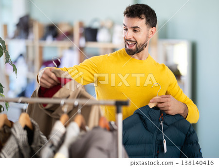 Young man chooses down jacket or raincoat Young man chooses down jacket or raincoat 138140416