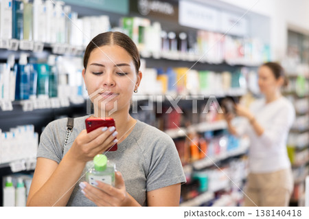 Woman shopper scanning a barcode on a cosmetics package with her phone. Searching for information via Internet Woman shopper scanning a barcode on a cosmetics package with her phone. Searching for information via Internet 138140418