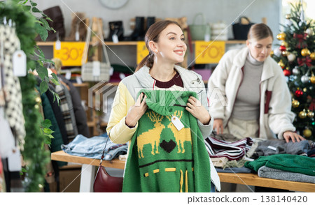 Positive young woman choosing sweater in clothing store Positive young woman choosing sweater in clothing store 138140420
