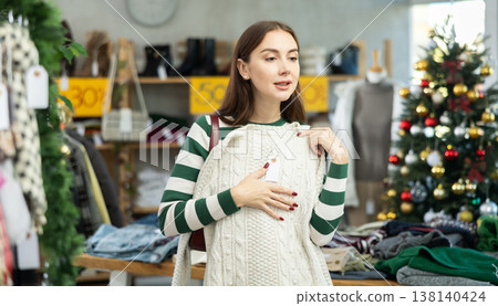 Woman standing in sale area and choosing a sweater Woman standing in sale area and choosing a sweater 138140424