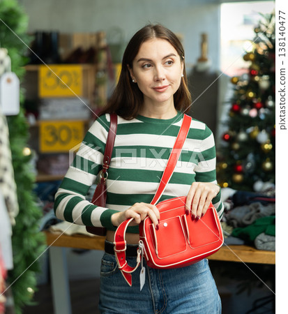 Positive young woman choosing handbag in clothing store Positive young woman choosing handbag in clothing store 138140477