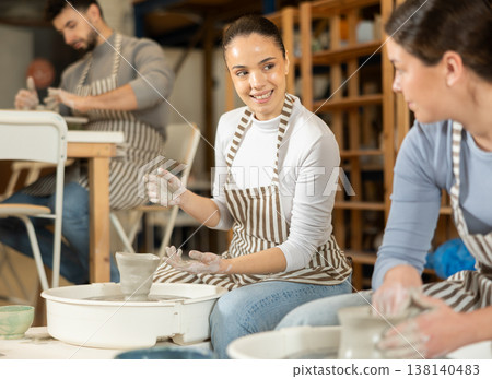 Girl working at pottery wheel and talking to girl Girl working at pottery wheel and talking to girl 138140483