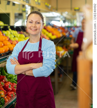Middle-aged saleswoman standing in front of counter in grocery store Middle-aged saleswoman standing in front of counter in grocery store 138140492
