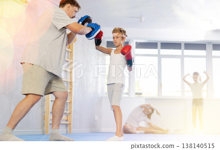 Boy and dad are boxing in gym, father helps child to work out force of blow. 138140515