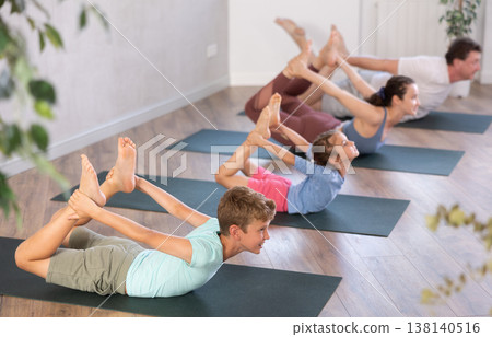 Diligent preteen boy practicing bow pose of yoga with his family Diligent preteen boy practicing bow pose of yoga with his family 138140516
