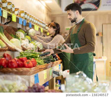Young male seller putting cucumbers on counter in grocery market 138140517