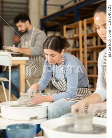 Two girls craftspersons busy molding clay products on pottery wheel Two girls craftspersons busy molding clay products on pottery wheel 138140525
