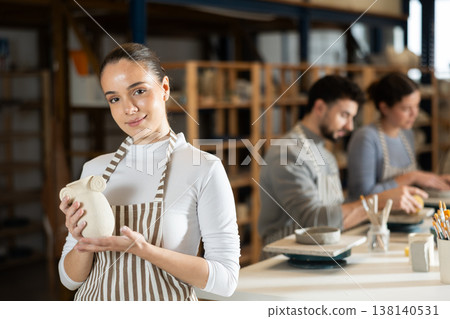 Girl stands in pottery workshop and shows created work, finished decorative vase Girl stands in pottery workshop and shows created work, finished decorative vase 138140531