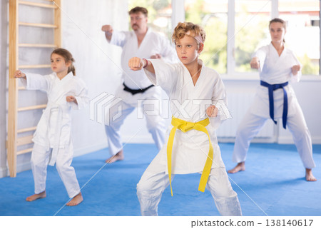 Preteen boy in kimono practicing punches as part of kata with family Preteen boy in kimono practicing punches as part of kata with family 138140617