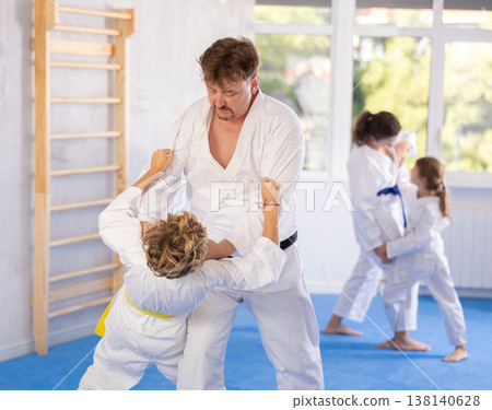 Judo or jiu jitsu classes - family with two children practicing grabbing and throwing on sports mats Judo or jiu jitsu classes - family with two children practicing grabbing and throwing on sports mats 138140628
