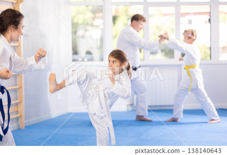Preteen girl in kimono practicing karate kicks during sparring with mother 138140643