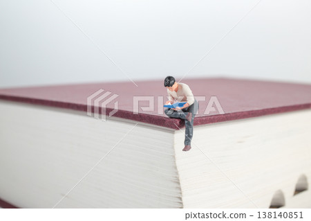 Miniature Figure Sitting on Oversized Book Reading Object Miniature Figure Sitting on Oversized Book Reading Object 138140851