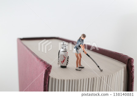 Miniature Golfer Practicing Shot on Oversized Book Surface 138140881