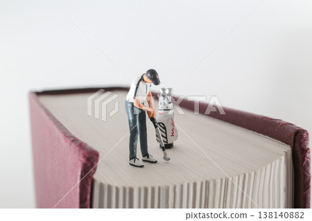 Miniature Golfer Preparing Shot on Oversized Book Surface 138140882