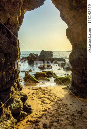 Golden hour sand beach seen through ancient arch rock formation Algarve Portugal Golden hour sand beach seen through ancient arch rock formation Algarve Portugal 138142429
