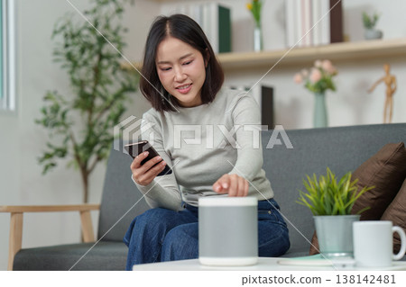 Woman using smartphone and smart speaker in modern living room 138142481