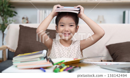 Smiling girl holding books on head during study time 138142494