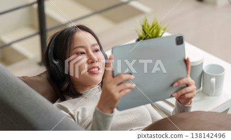 Woman using tablet and headphones while relaxing on couch Woman using tablet and headphones while relaxing on couch 138142496