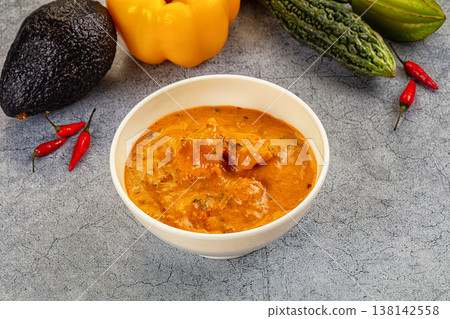 Spicy Indian chicken curry in a bowl with fresh vegetables and chili peppers. 138142558