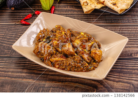 Bowl of traditional spicy chicken curma with flatbread, chilies, exotic vegetables on wood table. Bowl of traditional spicy chicken curma with flatbread, chilies, exotic vegetables on wood table. 138142566
