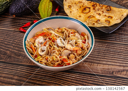 Stir-fried seafood noodles with shrimp and squid in a bowl on a wooden table. Stir-fried seafood noodles with shrimp and squid in a bowl on a wooden table. 138142567