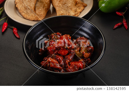 Spicy Chicken Indo-Chinese appetizer with a rich, glossy red sauce on a beige plate, set on a dark tabletop. Spicy Chicken Indo-Chinese appetizer with a rich, glossy red sauce on a beige plate, set on a dark tabletop. 138142595