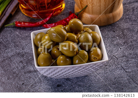 Bowl of marinated green olives with red chili peppers and oil on a dark textured background Bowl of marinated green olives with red chili peppers and oil on a dark textured background 138142613