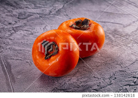 Two fresh ripe orange persimmons on a grey textured surface 138142618