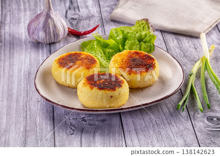 Golden fried potato patties served with fresh lettuce, garlic, and spring onions on a rustic wooden table. 138142623