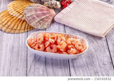 Cooked peeled shrimp in a ceramic bowl on a rustic gray wooden table with a seashell. 138142632