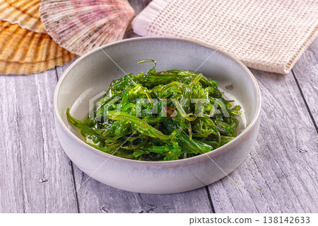Japanese seaweed salad Chuka with sesame seeds and chili in a white bowl on a wooden table. 138142633