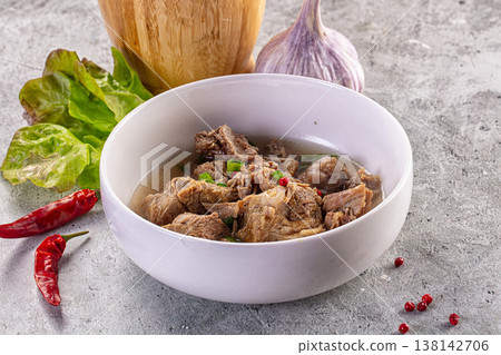 Savory meat and bone broth soup in a white bowl with garlic, chili, and herbs on a rustic grey table Savory meat and bone broth soup in a white bowl with garlic, chili, and herbs on a rustic grey table 138142706
