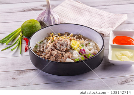 Vietnamese pho bo soup with beef, rice noodles and fresh herbs on a white wooden table 138142714