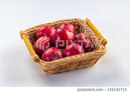 Ripe red plums in a rustic wicker basket on a clean white background. Ripe red plums in a rustic wicker basket on a clean white background. 138142715