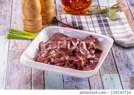Raw chicken liver in a white dish on a rustic wooden table with spices and fresh green onions for cooking. Raw chicken liver in a white dish on a rustic wooden table with spices and fresh green onions for cooking. 138142716