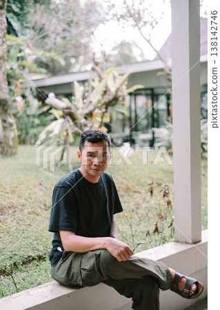 Portrait of Asian Man Sitting Relaxed Outdoors Looking at Camera Portrait of Asian Man Sitting Relaxed Outdoors Looking at Camera 138142746