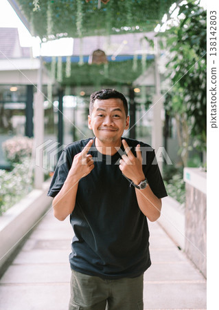 Casual man pointing at his face showing how to smile in outdoor setting Casual man pointing at his face showing how to smile in outdoor setting 138142803
