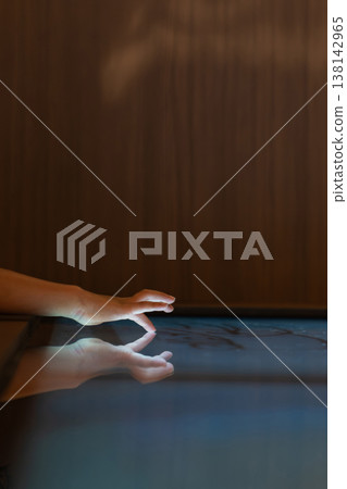 Child hand touching an illuminated interactive surface with reflection representing human connection with technology and digital interaction. Child hand touching an illuminated interactive surface with reflection representing human connection with technology and digital interaction. 138142965