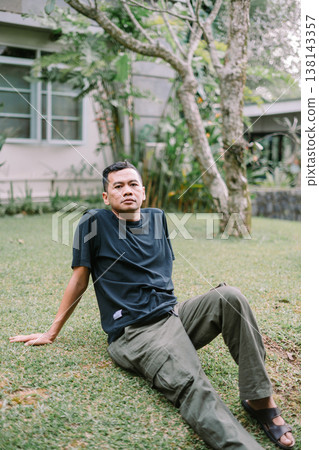 Portrait of Relaxed Asian Man Sitting on Grass Outdoors Portrait of Relaxed Asian Man Sitting on Grass Outdoors 138143357