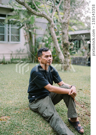 Asian Man Sitting on Grass Looking Up Feeling Free and Relaxed 138143358