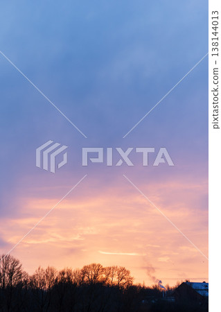 Dramatic pastel sunset sky above dark winter trees and distant buildings Dramatic pastel sunset sky above dark winter trees and distant buildings 138144013