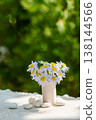 Small White and Purple Daisy Flowers in Vase on Table with Green Bokeh Background 138144566
